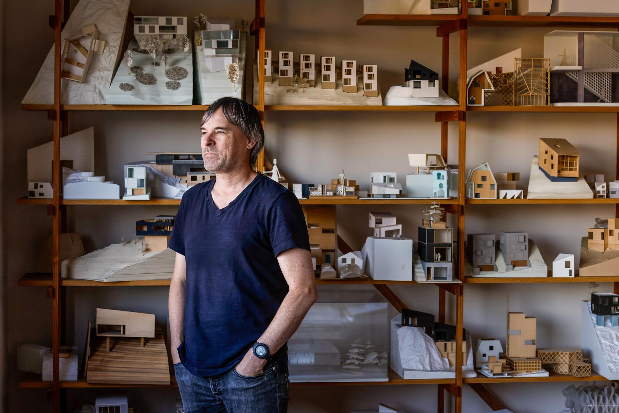 Simon Storey stands in his home office, where miniature models fill a wall-sized shelf.