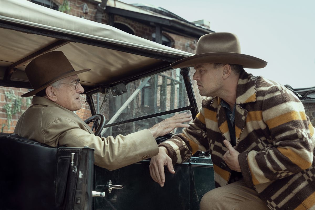 Killers of the Flower Moon'da kovboy şapkası ve pançosuyla Leonardo DiCaprio, Robert DeNiro'nun kullandığı bir otomobilin üzerine eğiliyor.