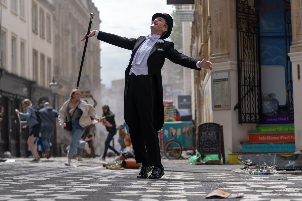Neil Patrick Harris danst in een smoking met jaspanden, hoge hoed en wandelstok terwijl er achter hem chaos uitbreekt in de straten van Londen in de Doctor Who-special 'The Giggle'