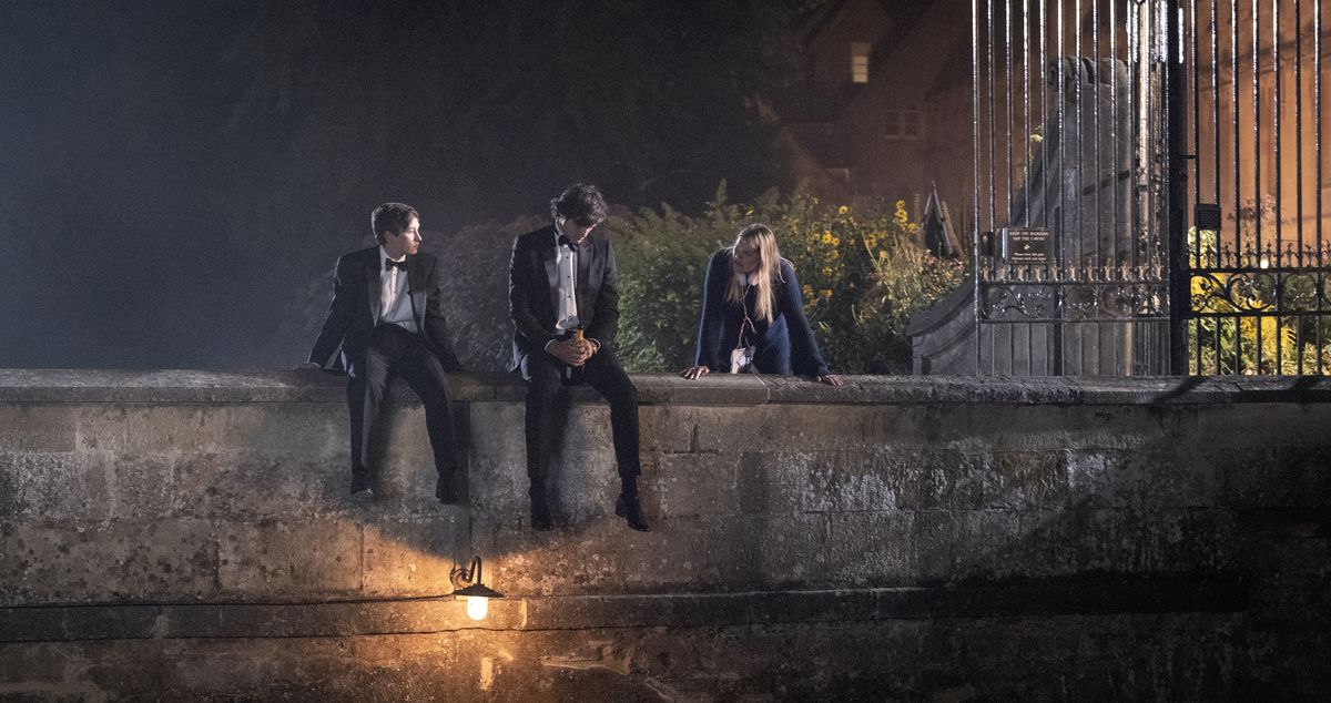 Oliver (Barry Keoghan) und Felix Catton (Jacob Elordi) sitzen im Smoking zusammen auf einer kleinen Steinbrücke über einem Teich, während Venetia (Alison Oliver) in der Nähe in Saltburn steht