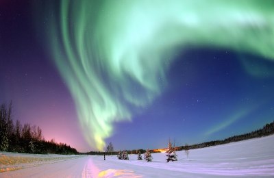 Karlı bir manzara üzerinde koyu mor ve siyah gün batımına karşı mavi-yeşil bir aurora