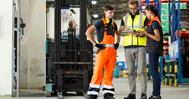 工場で iPad を見ながら会話する 3 人のエンジニア
