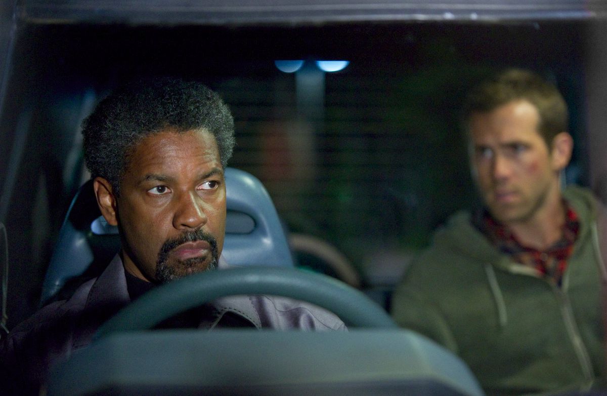 Tobin Frost (Denzel Washington), arka planda Matt Weston (Ryan Reynolds) ile bir minibüsün ön koltuğunda oturuyor.