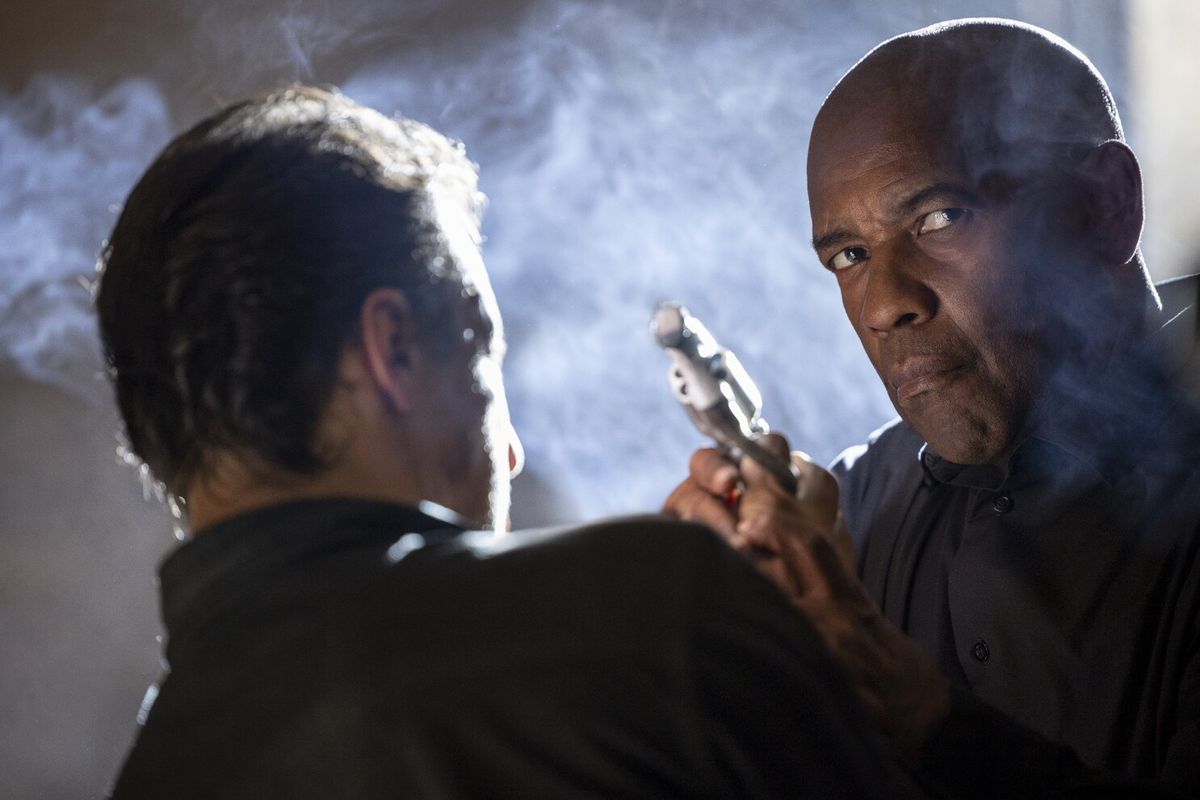 Denzel Washington trong vai Robert McCall chĩa súng lục qua vai một người đàn ông trong The Equalizer 3.