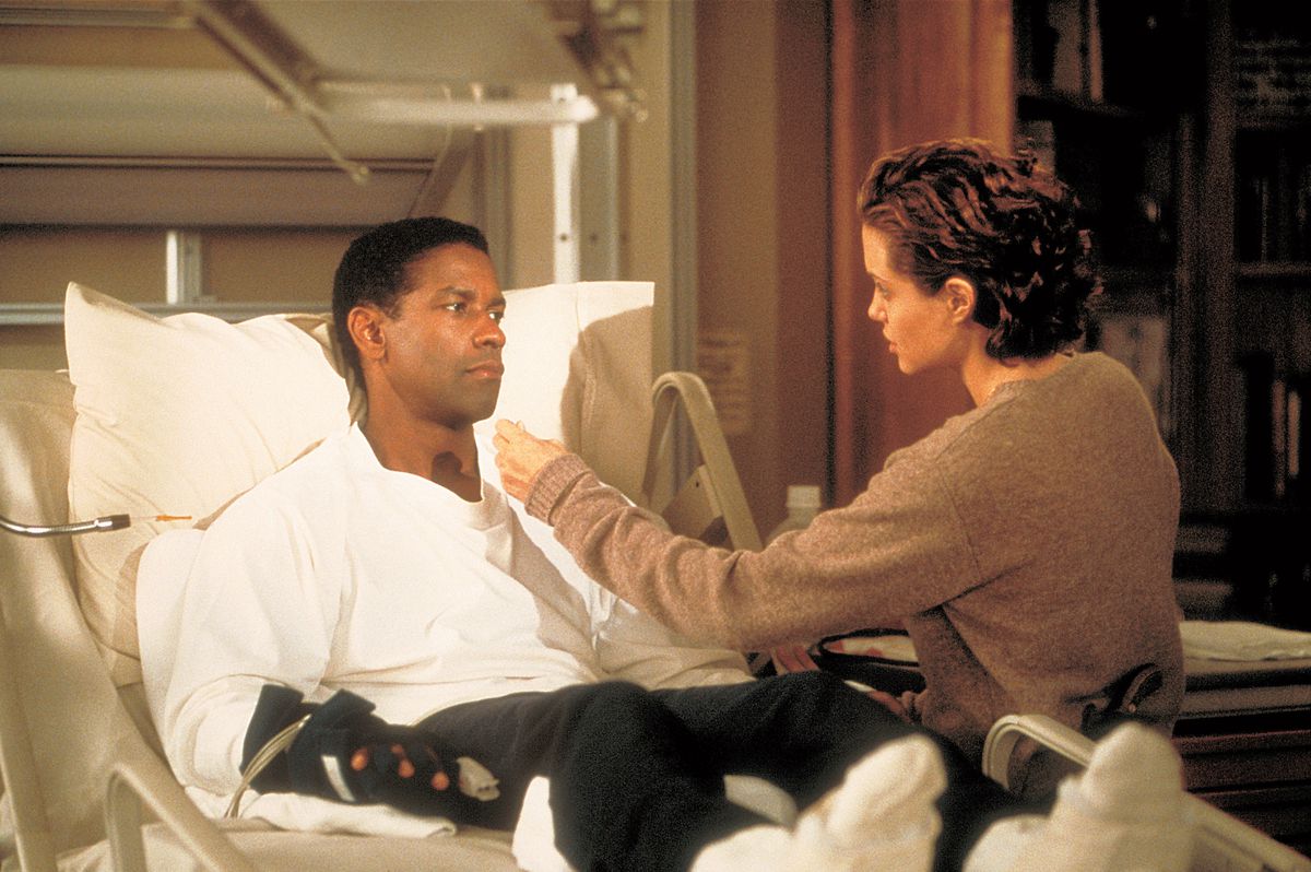 Angelina Jolie sentada en una cama de hospital en la que yace Denzel Washington, en The Bone Collector.