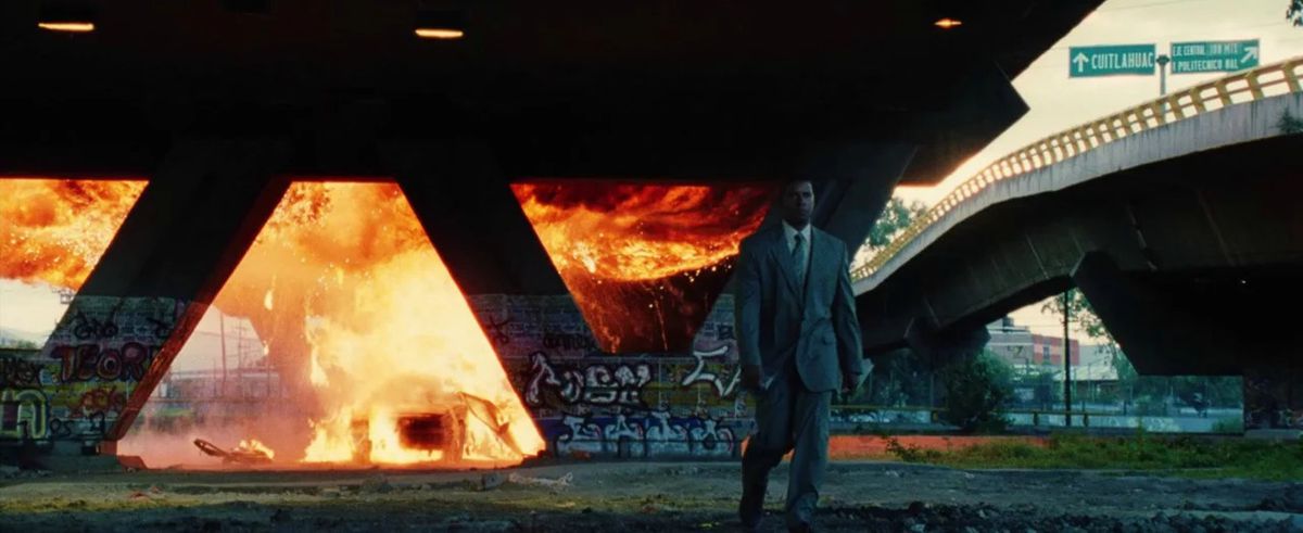 『マン・オン・ファイア』で、高速道路の地下道の下で炎に包まれた車から離れて歩いているクリージー。