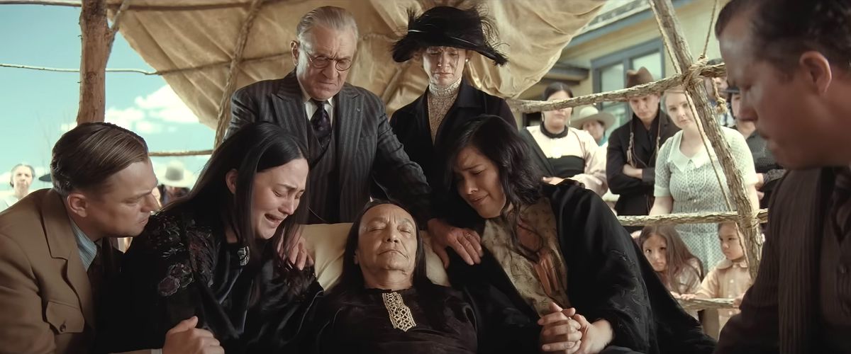 Ernest (Leonardo DiCaprio), Mollie (Lily Gladstone), King (Robert De Niro), Martha (Sarah Spurger) and others gather around the body of Mollie’s mother to mourn in an open-sided outdoor shelter in Killers of the Flower Moon