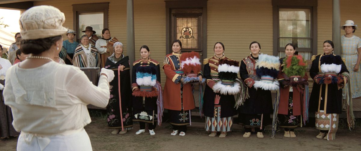 Mollie (Lily Gladstone), in abito formale tradizionale Osage, sta con un gruppo di altre donne native vestite a festa, in posa per una foto in Killers of the Flower Moon