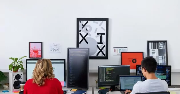 Twee ontwikkelaars zitten in bureaustoelen met uitzicht op de muur en werken op computers