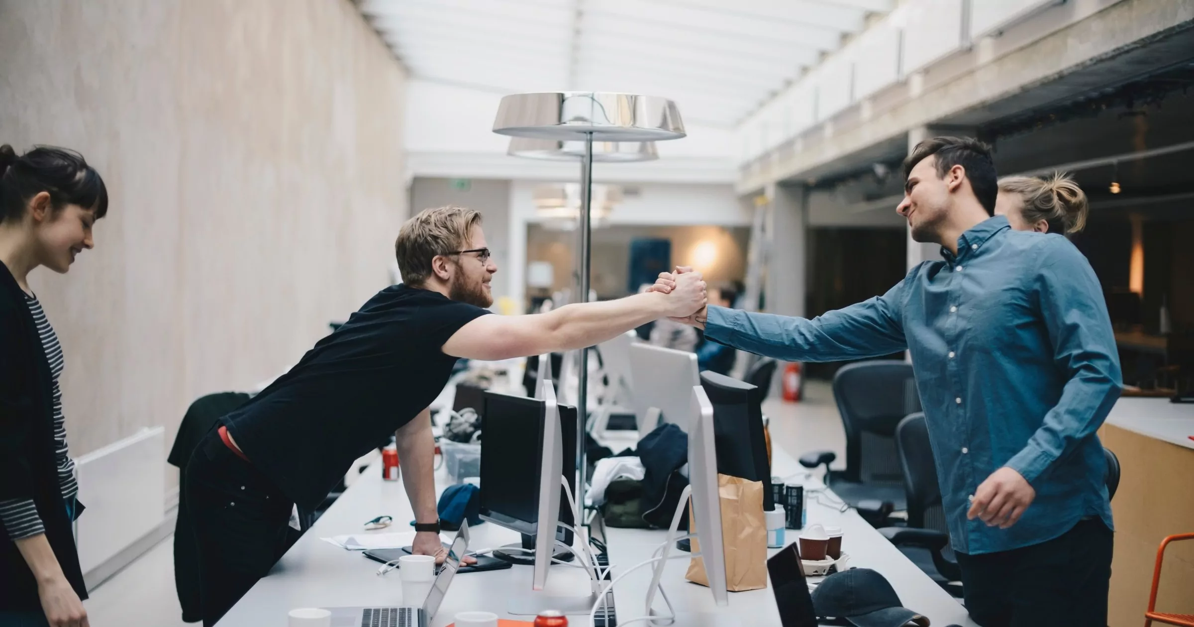 Male computer programmers holding hands over desk in office celebrating a successful digital transformation strategy step