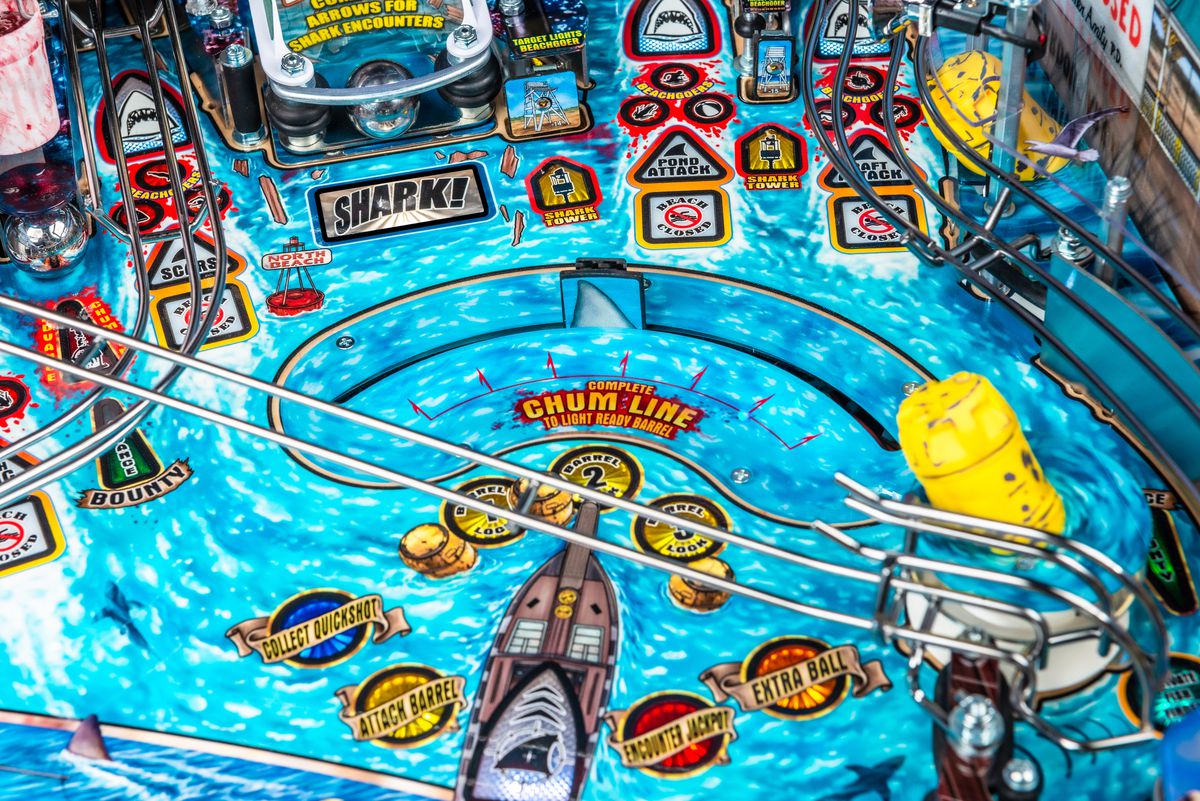 A close up photograph of the playfield of the pinball table Jaws, focused on the “Chum Line” area with a fin-shaped moving target