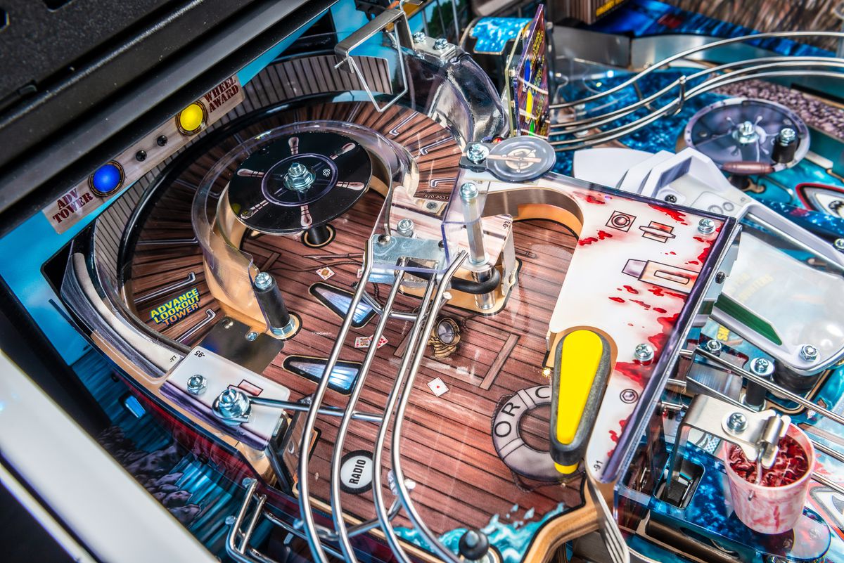 Een close-upfoto van het speelveld van de flipperkast Jaws, gefocust op het verhoogde speelveld dat de Orca-vissersboot en uitkijktoren voorstelt