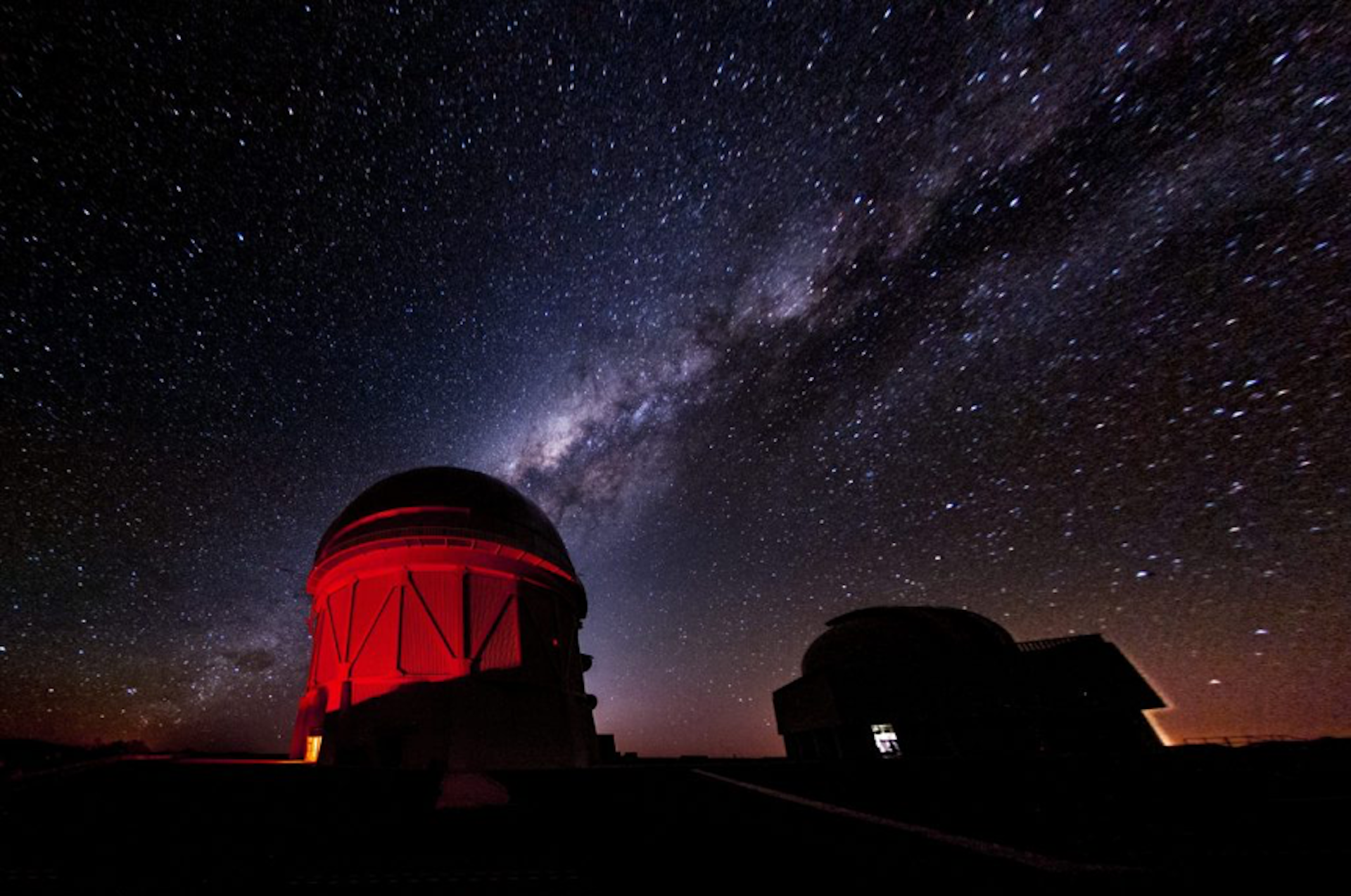 Een foto van een rood verlicht observatoriumgebouw met de sterrenhemel op de achtergrond.