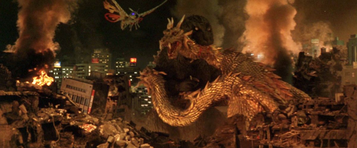 Godzilla bijt in de nek van koning Ghidorah met een verwoeste stad op de achtergrond en Mothra vliegt naar hen toe.
