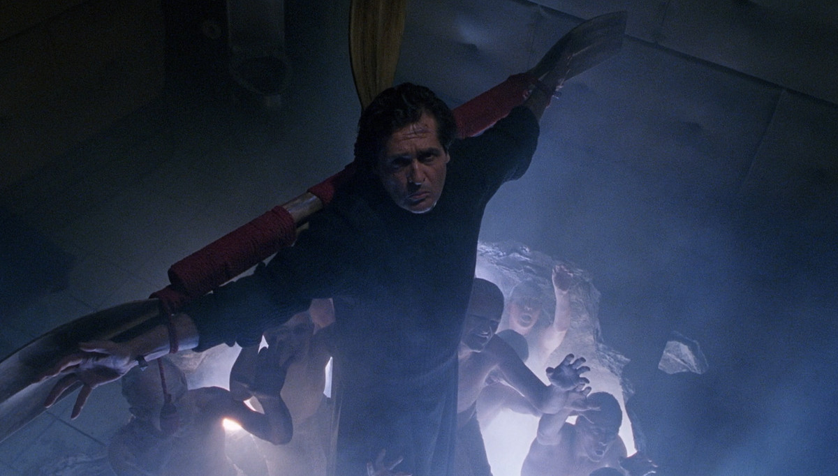 A priest hangs on a cross over an open portal with demon hands coming out in the exorcist 3