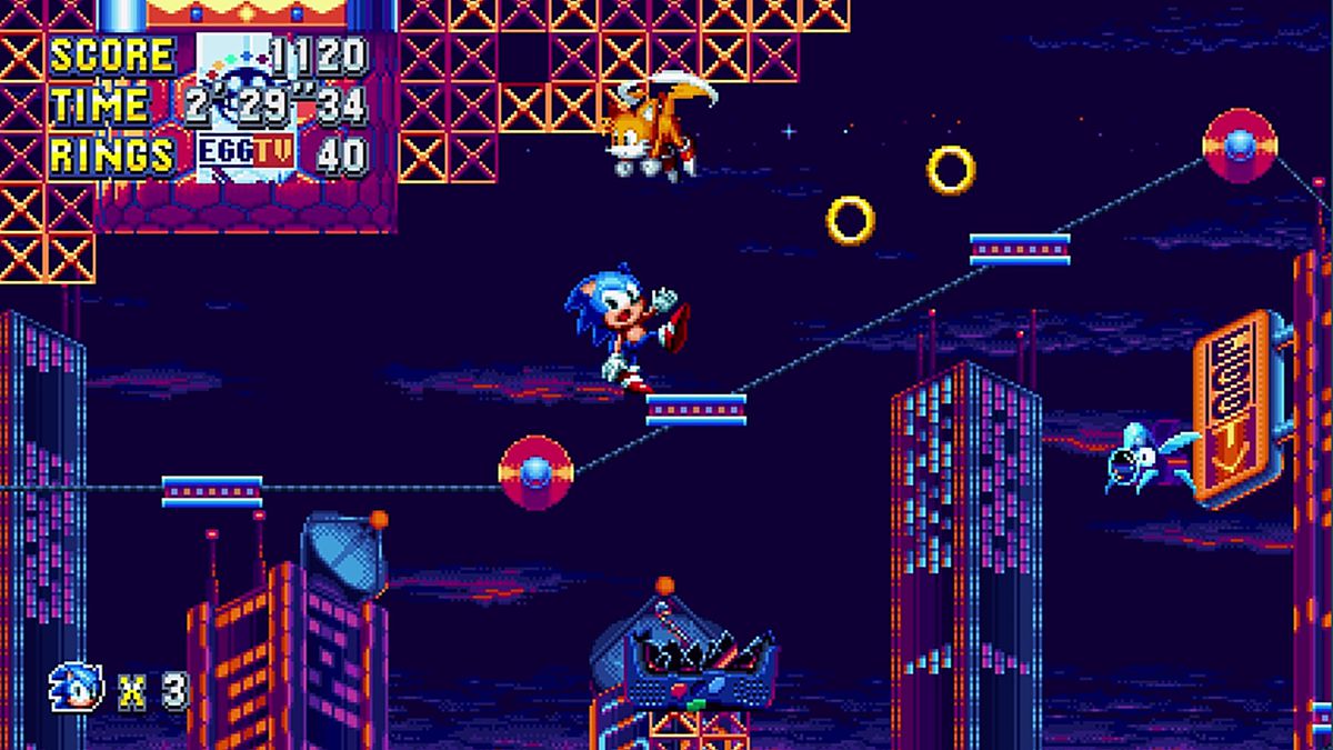 Sonic Mania의 스크린샷에서 Tails가 머리 위로 맴돌고 있는 동안 Sonic the Hedgehog는 움직이는 플랫폼에서 위태롭게 균형을 잡고 있습니다.