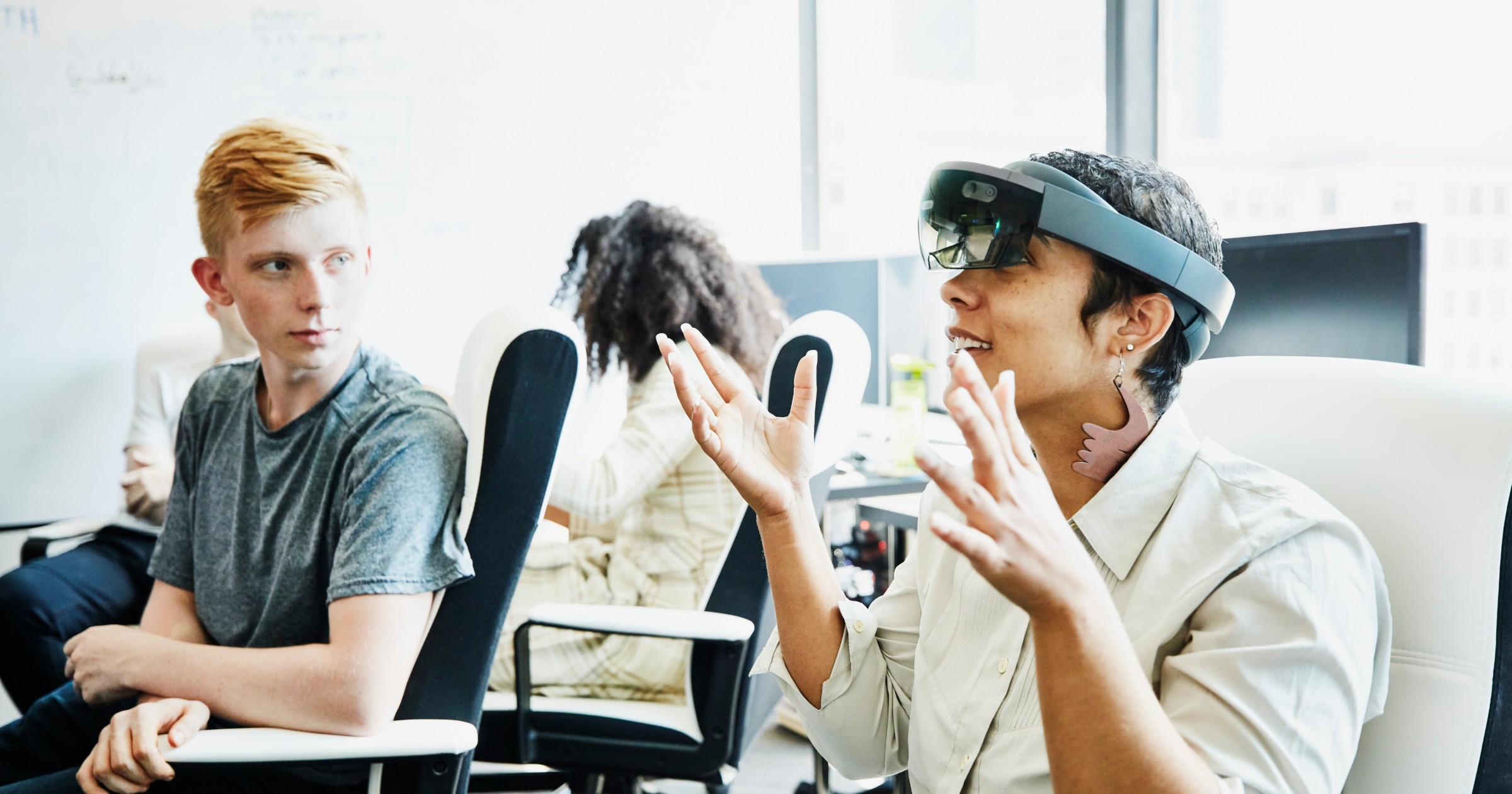 Vrouwelijke ingenieur in gesprek met collega tijdens het testen van programma op augmented reality-headset in computerlokaal