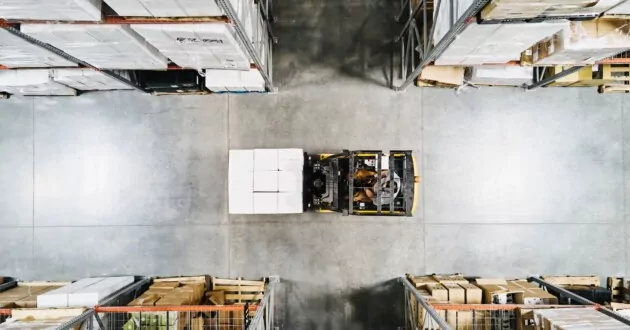 Vista aérea del trabajador del almacén moviendo paletas de mercancías con una carretilla elevadora en el almacén