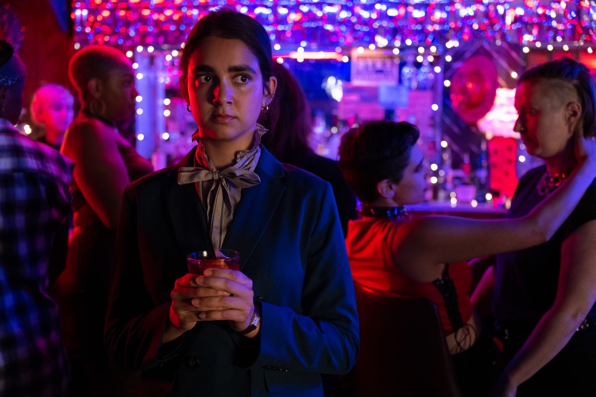 Marian clutches her drink with both hands and looks on nervously in a lesbian bar scene from Drive-Away Dolls