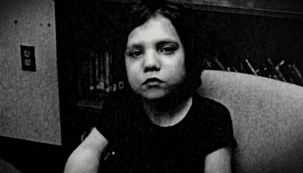 Zwart-wit beeld van Natalia, een jong blank meisje met donker haar, geknipt in een stompe bob, en een neutrale uitdrukking op haar gezicht.