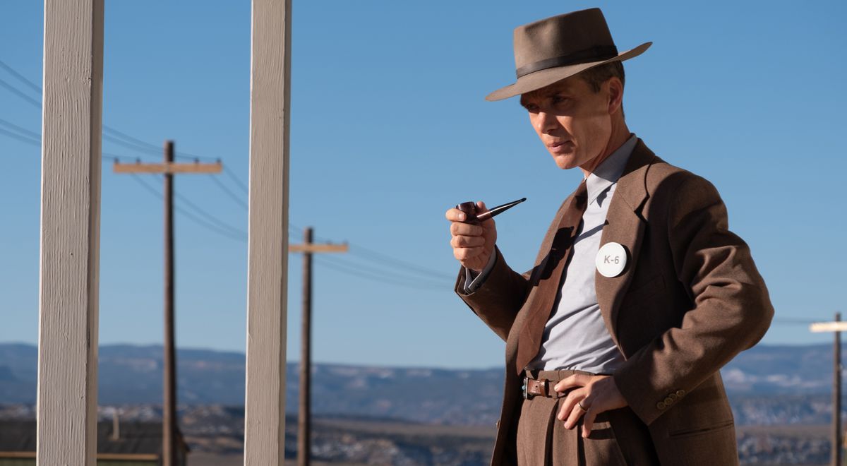 J. Robert Oppenheimer (Cillian Murphy), in bruin pak en hoed, houdt een pijp vast en staat in een woestijn bij een rij telefoonpalen in Christopher Nolan's Oppenheimer