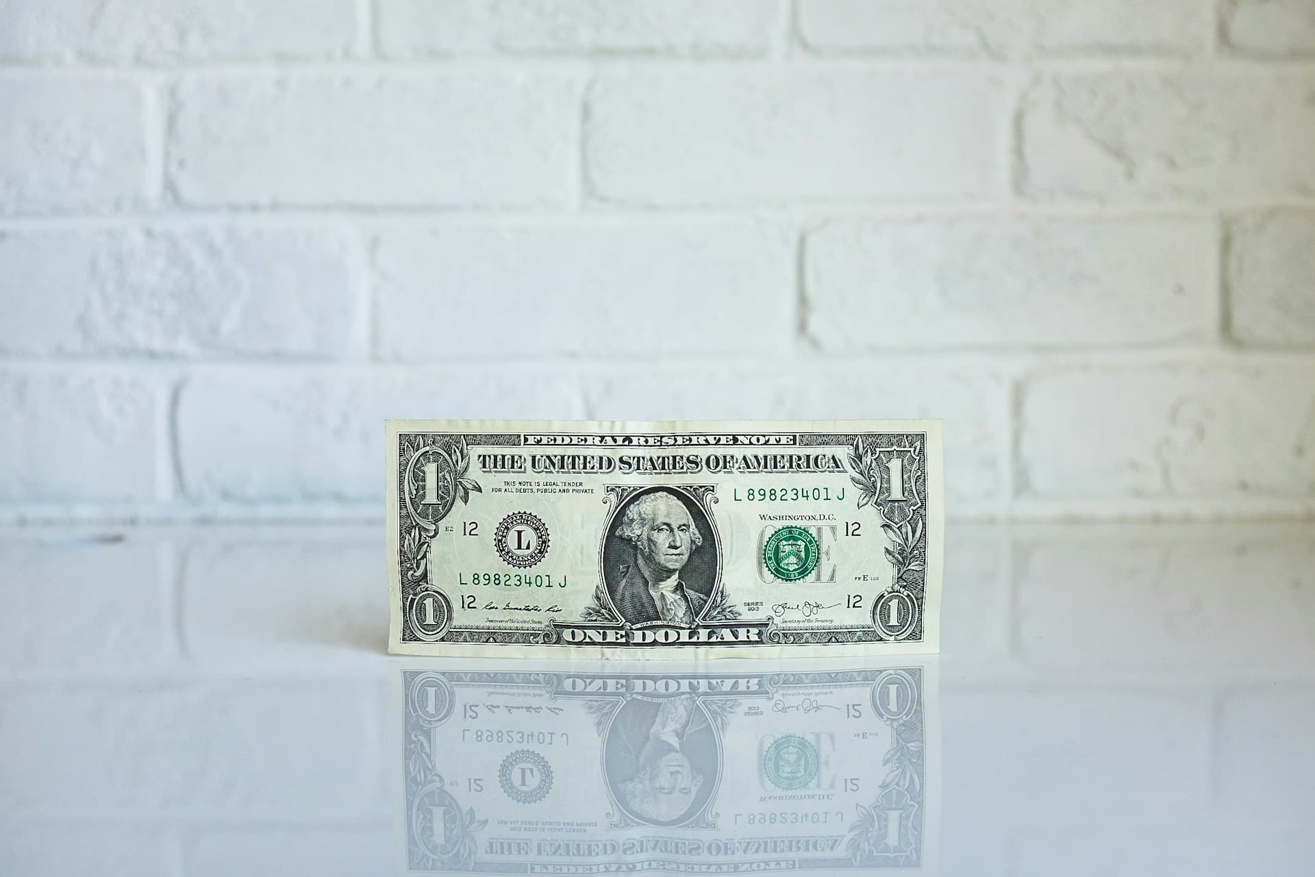Een enkel dollarbiljet met het gezicht van George Washington erop, tegen een witte bakstenen muur