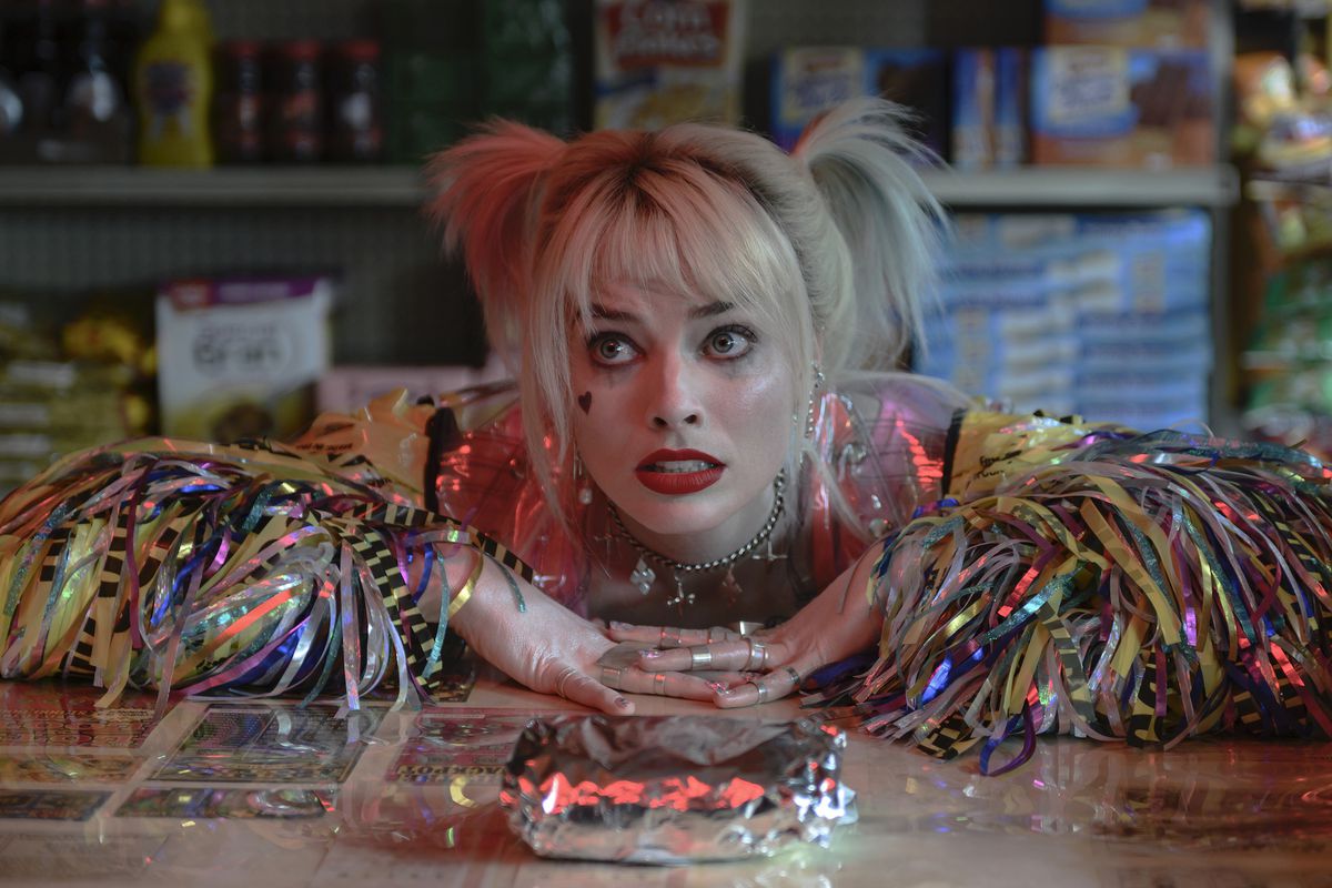 Margot Robbie apoya los brazos en un mostrador de delicatessen y mira suplicante su sándwich de desayuno como Harley Quinn en Birds of Prey.