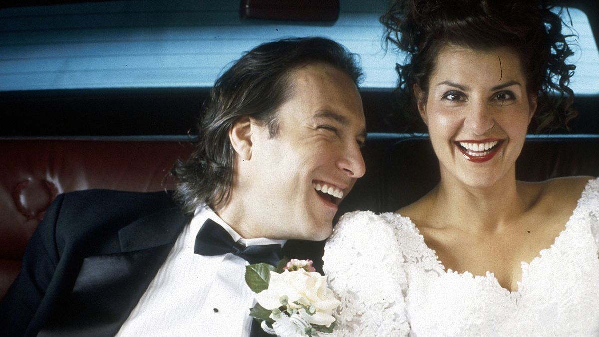 Ian (John Corbett) and Toula (Nia Vardalos) laugh in the backseat of a car in a screenshot from My Big Fat Greek Wedding