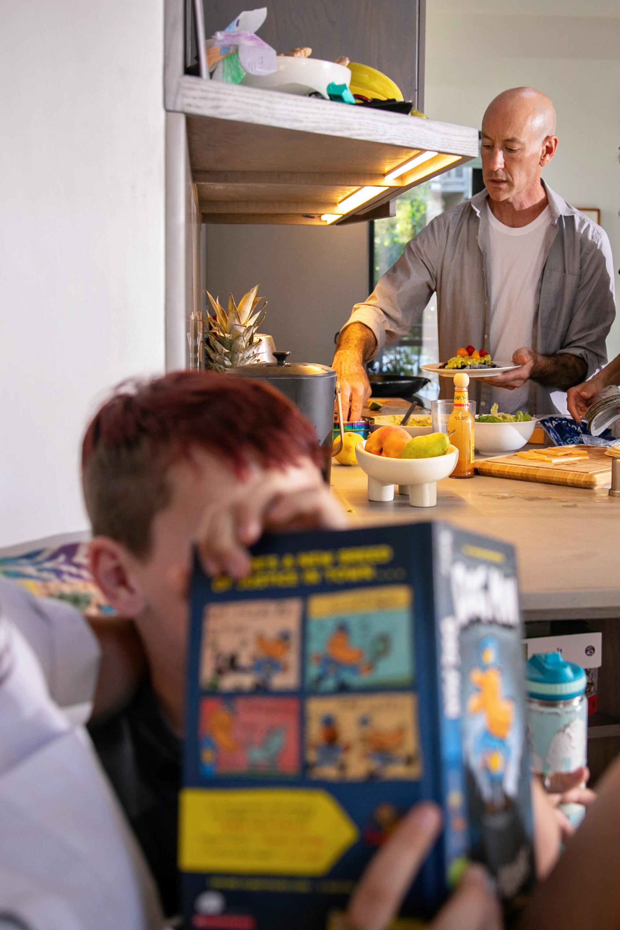 一名男子在厨房准备晚餐，而一名孩子则在附近的角落里读书。