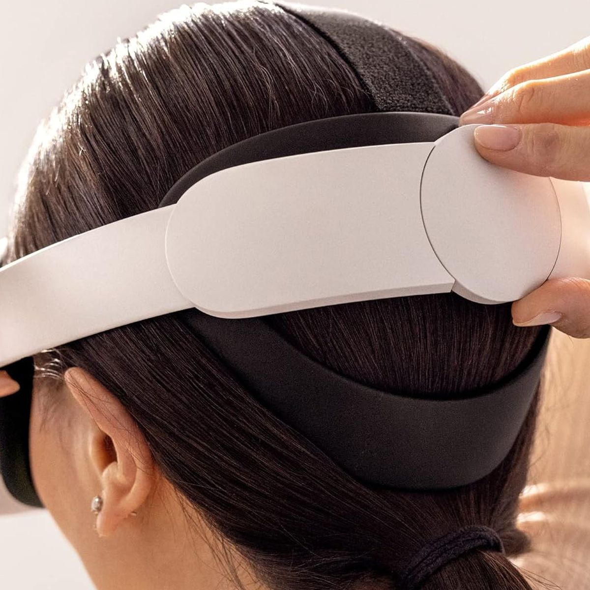 Ein Foto, das ein Modell zeigt, das den Elite-Gurt am Meta Quest 2 Virtual-Reality-Headset anpasst. Das Headset wird auf dem Kopf befestigt und der Benutzer dreht ein Rädchen, um die Passform zu verbessern.