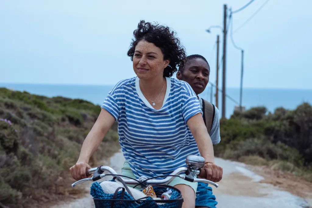 Una mujer montada en la parte trasera de una bicicleta mientras otra mujer pedalea y sonríe.