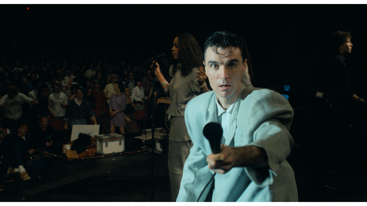 Stop Making Sense'de kendine özgü kostümü giyen David Byrne mikrofonu kameraya doğru tutuyor.