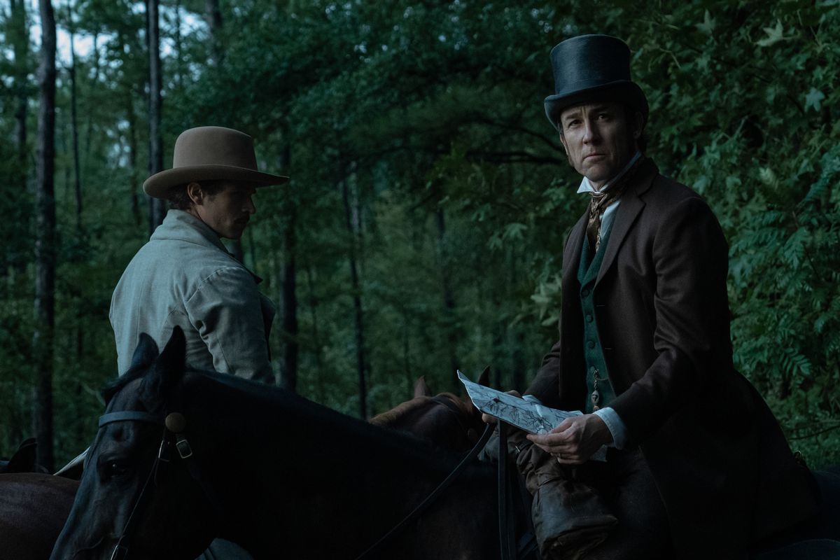 Stanton (Tobias Menzies) in groppa a un cavallo nel bosco guarda con curiosità fuori campo