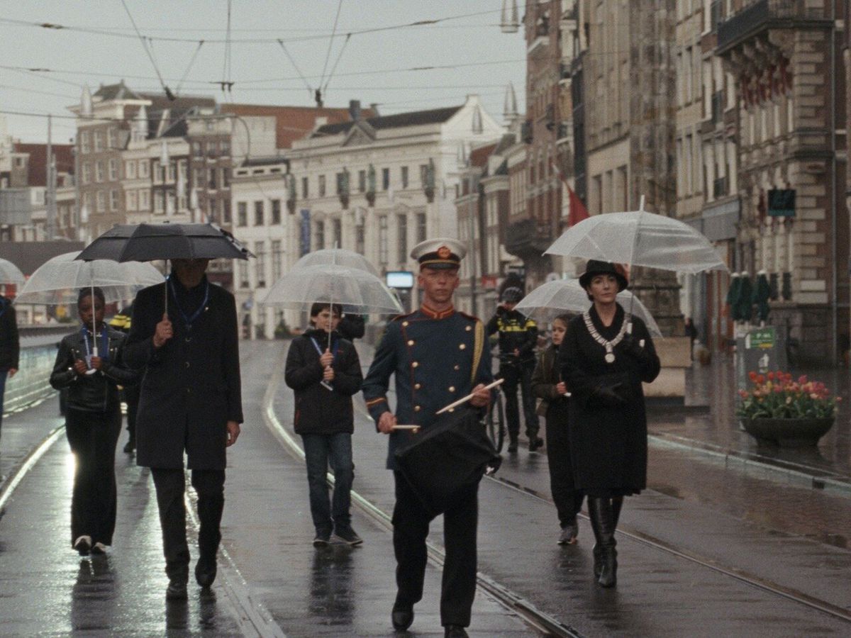 een archiefbeeld van een groep mensen met paraplu's achter een drummer die door een lege straat loopt.
