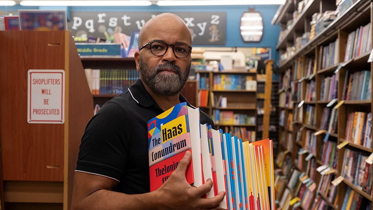 Ein kahlköpfiger Mann mit Brille und Bart hält einen Stapel Bücher in einem Buchladen.