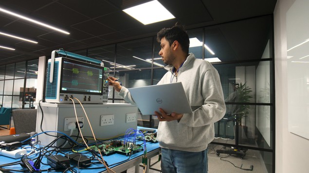 En mann i hettegenser jobber med en bærbar PC og et kvantesystem