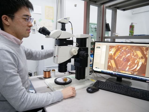 Foto von Takasada Shibauchi in seinem Labor, der auf einen Bildschirm neben einem Mikroskop blickt