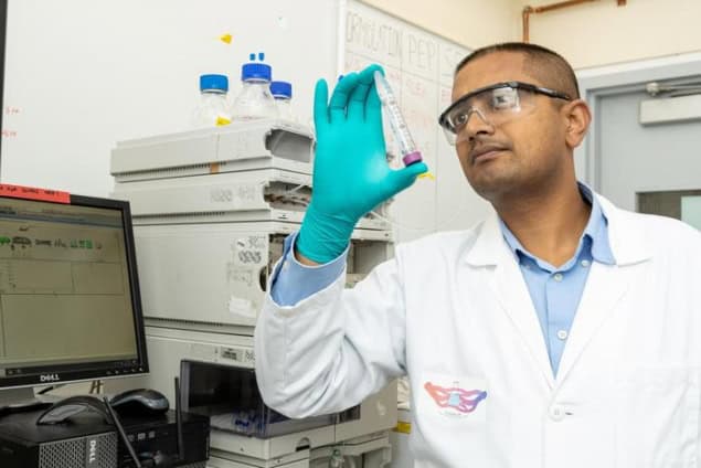 Photo of Vivek Kumar in a lab coat, safety goggles and gloves holding a glass vial containing the hydrogel