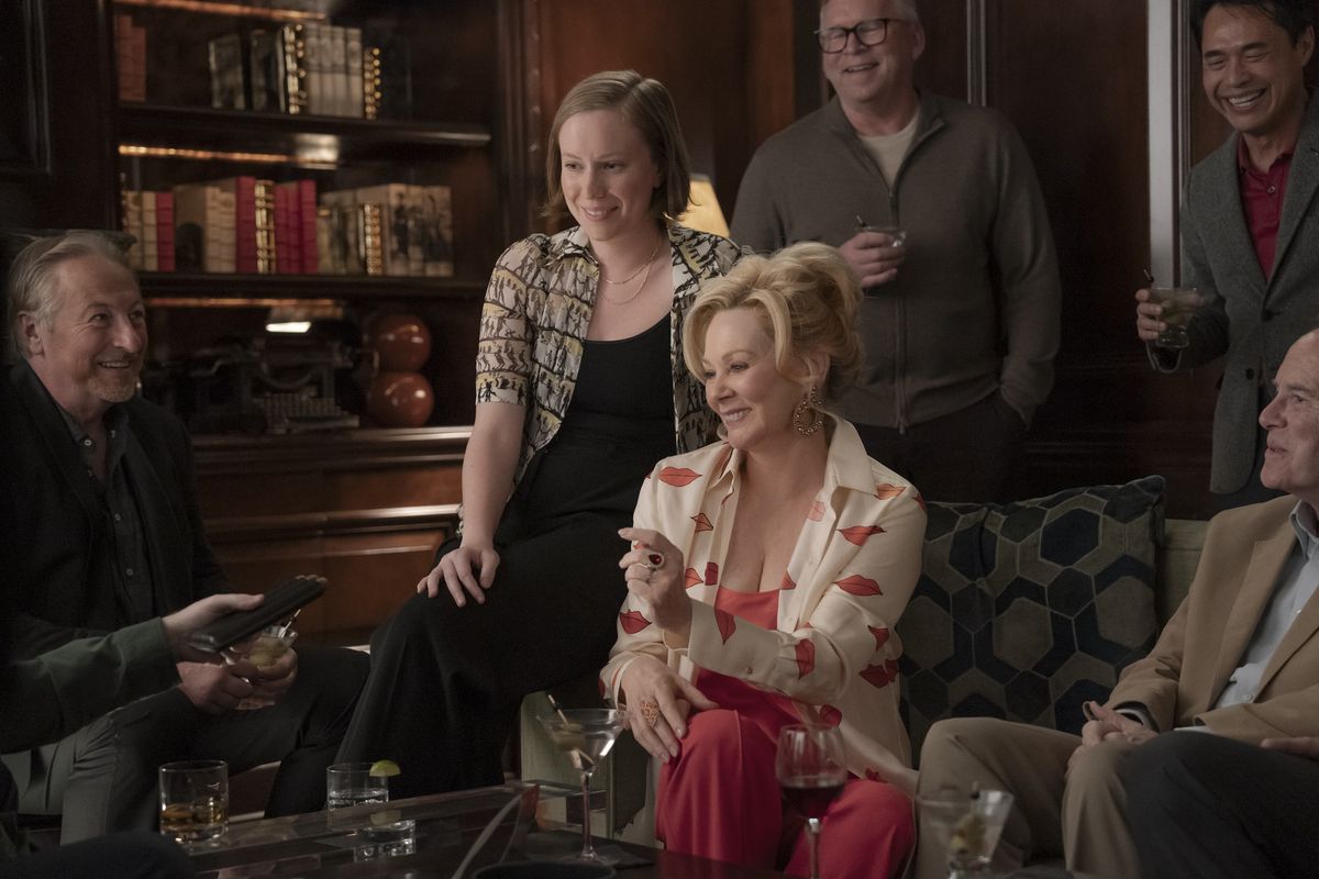 Deborah (Jean Smart) sits smiling with Ava (Hannah Einbinder) on the arm of her chair in a still from Hacks
