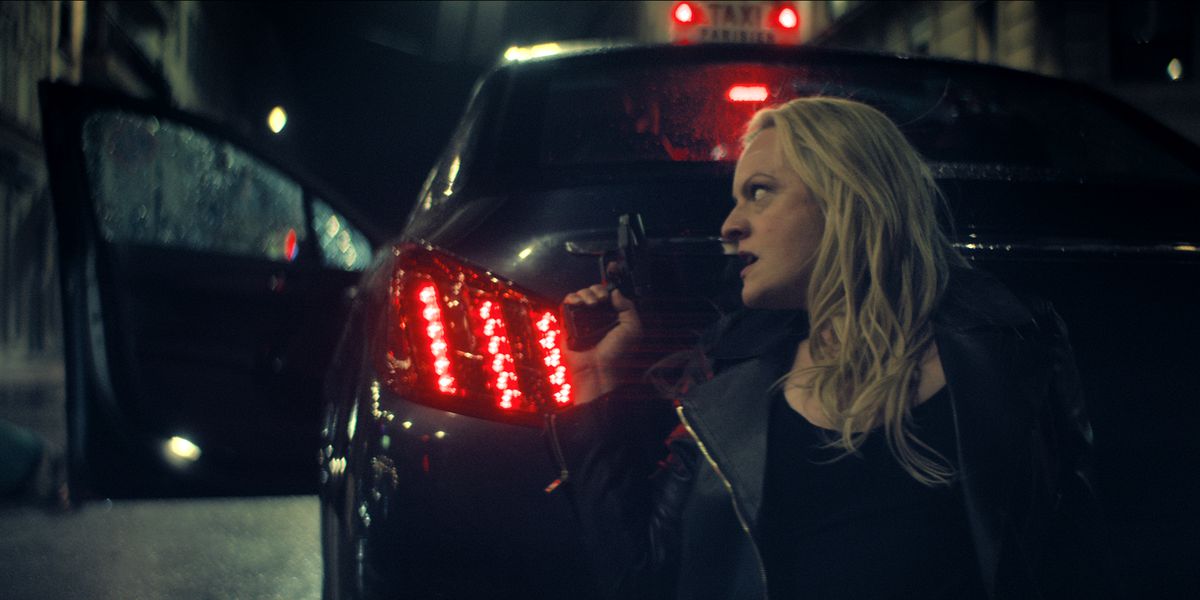 Imogen (Elisabeth Moss) kneeling behind a car with a gun out
