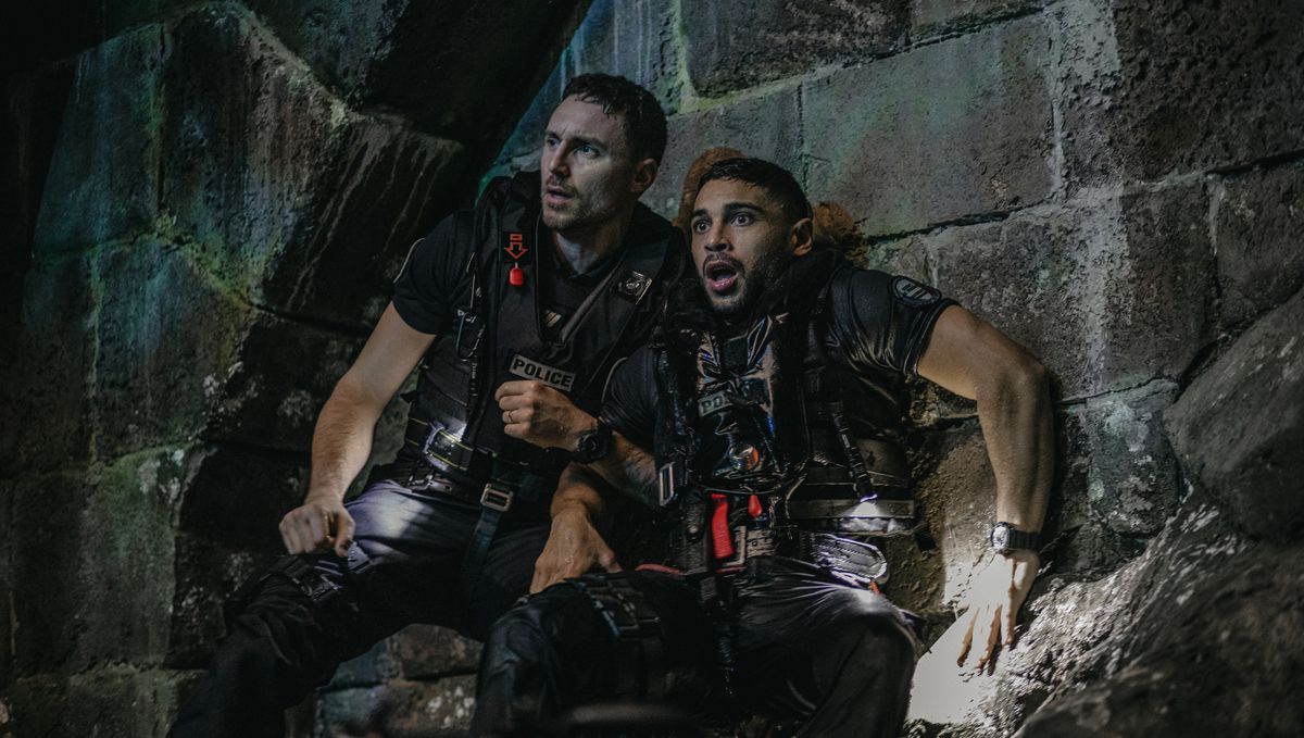 Police sergeant Adil (Nassim Lyes) and a fellow cop, both soaking wet and wearing tactical gear, press themselves up against a stone wall in an underground Parisian cistern in Xavier Gens’ Netflix shark thriller Under Paris