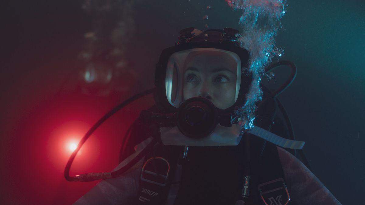Sophia (Bérénice Bejo) in a closeup, diving underwater at night in dark water with a bright red light behind her in Xavier Gens’ Netflix shark thriller Under Paris