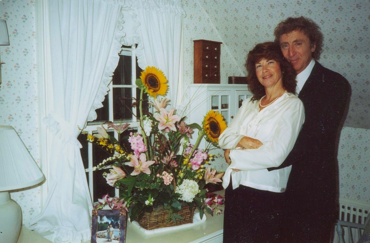Archival photo of Gene Wilder standing in a room with a woman next to a large bouquet of flowers in Remembering Gene Wilder.