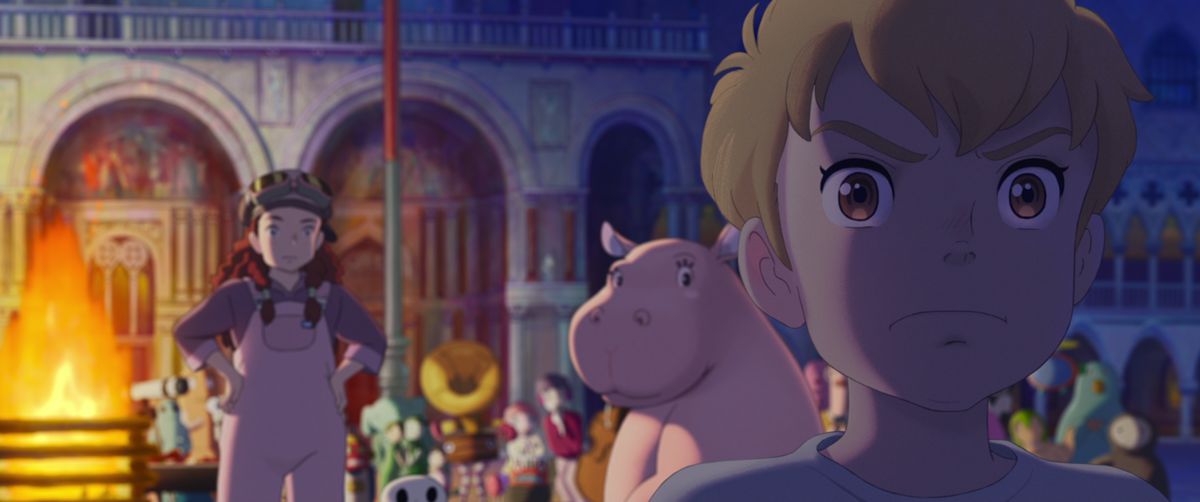 Imaginary friend Rudger, a blond boy with big brown eyes, frowns in the extreme foreground of a frame from Studio Ponoc’s The Imaginary, as a girl in pink overalls and aviator goggles and a pink hippo stand behind him in an outdoor arena