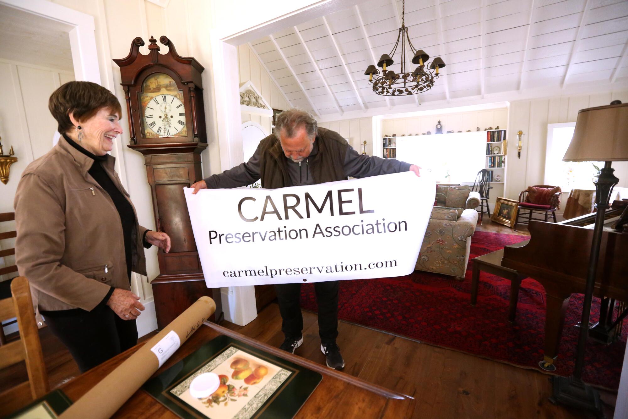 A woman smiles as a man unveils a sign that says Carmel Preservation Association. 